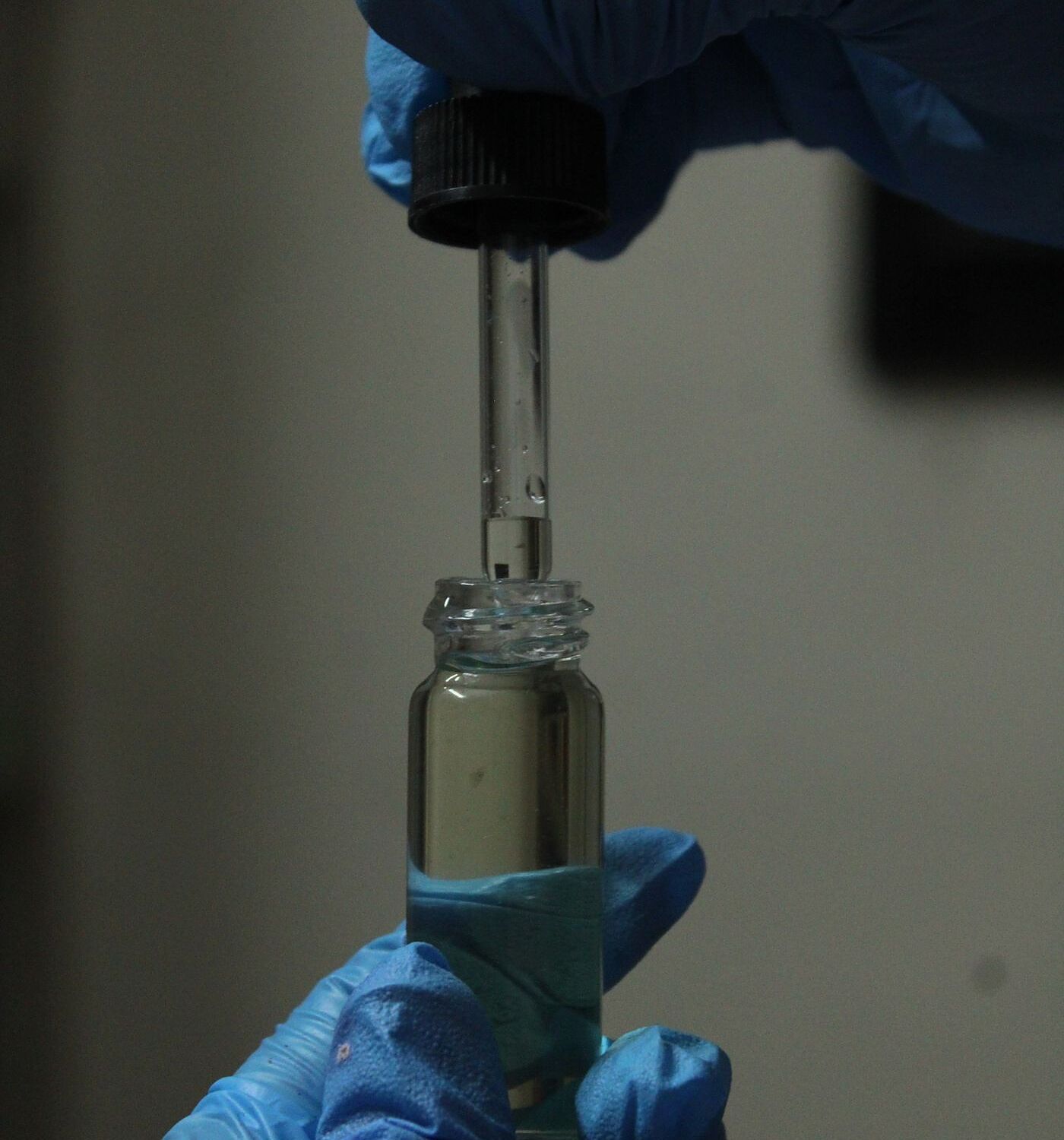A gloved hand holding a sealed amber vial